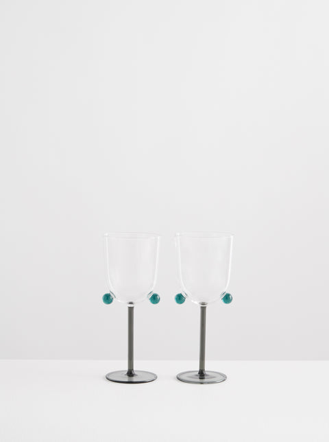 Two Maison Balzac wine glasses with teal colored pom poms and stem.