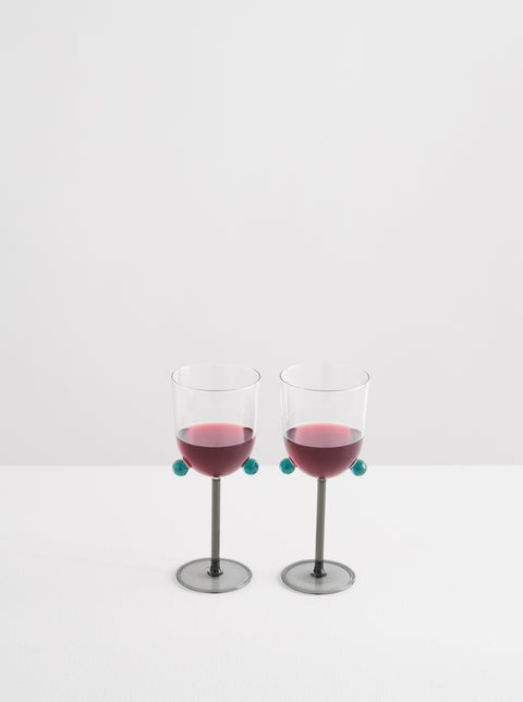 Two Maison Balzac wine glasses holding red wine with pompom detail.